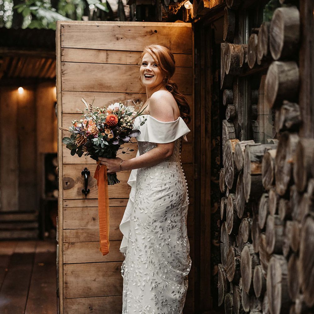 Bride off the shoulder floral embellished Love Spell wedding dress and carries Autumnal floral bouquet 