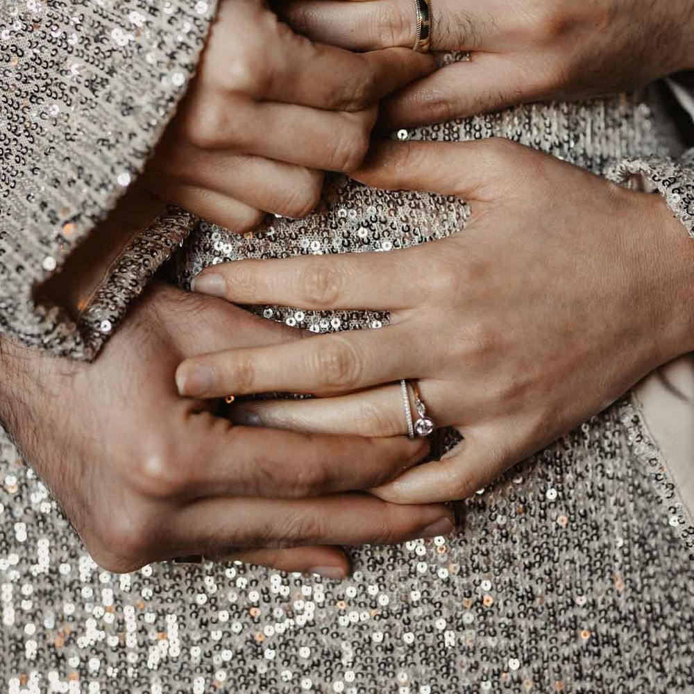 Modern luxe wedding rings holding hands against silver sparkly dress 