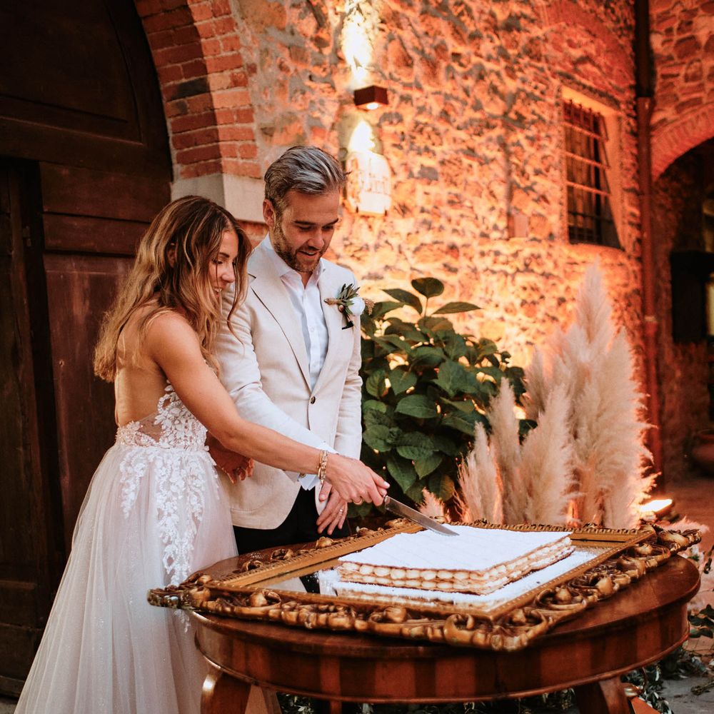 Bride in sparkly wedding dress with groom cutting the wedding cake at outdoor wedding reception