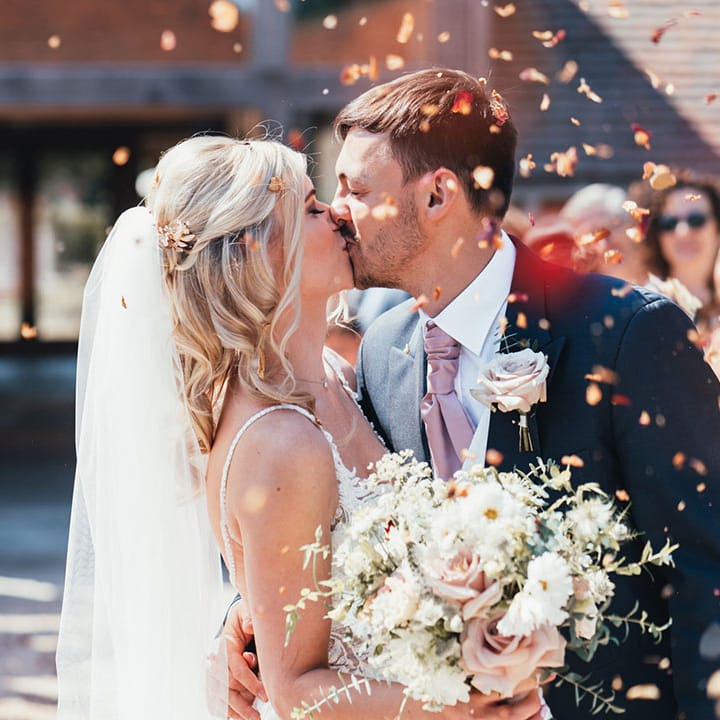The bride and groom share a kiss together as confetti is thrown around them 