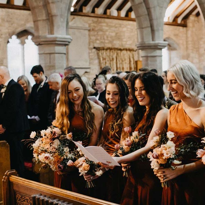 Bridesmaids in one shoulder burnt orange bridesmaid dresses in the alter of Brinsop Court wedding venue 