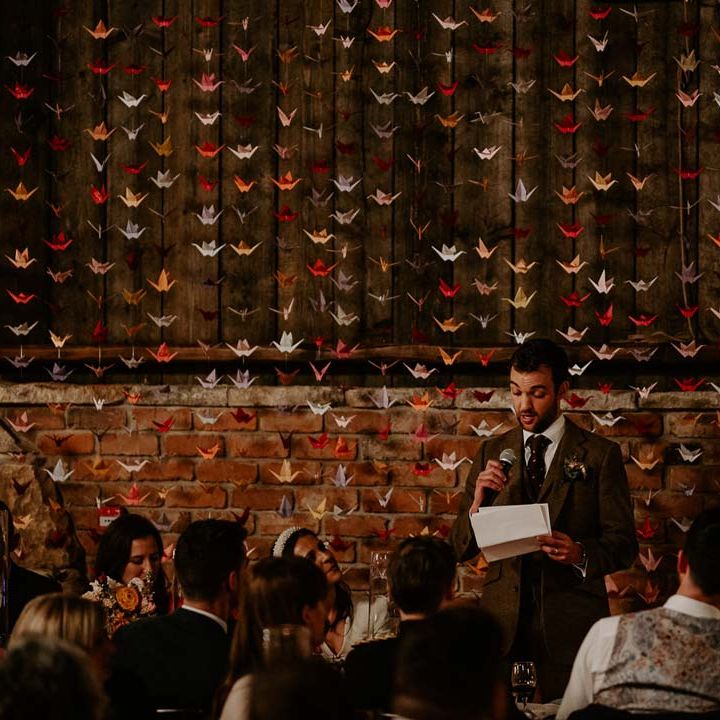 Groom doing grooms speech standing in front of 1000 origami paper cranes DIY wedding decor at Willow Marsh Farm Loughborough 
