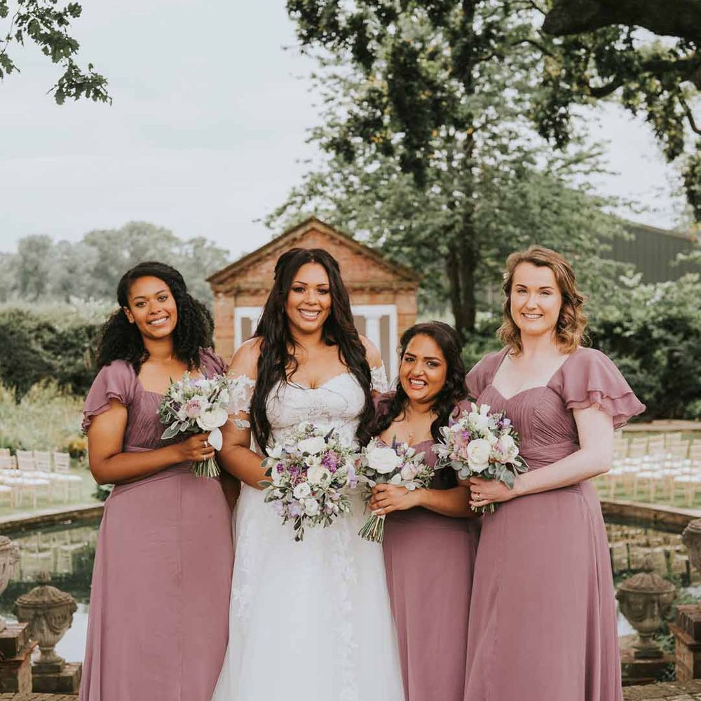 Bride in off the shoulder lace wedding dress standing with bridesmaids in square neck short sleeve dusky pink bridesmaid dresses 