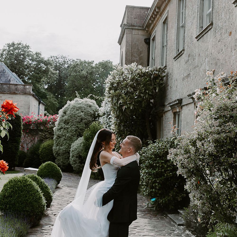 Groom in tuxedo lifting the bride as they share a kiss at country house wedding 