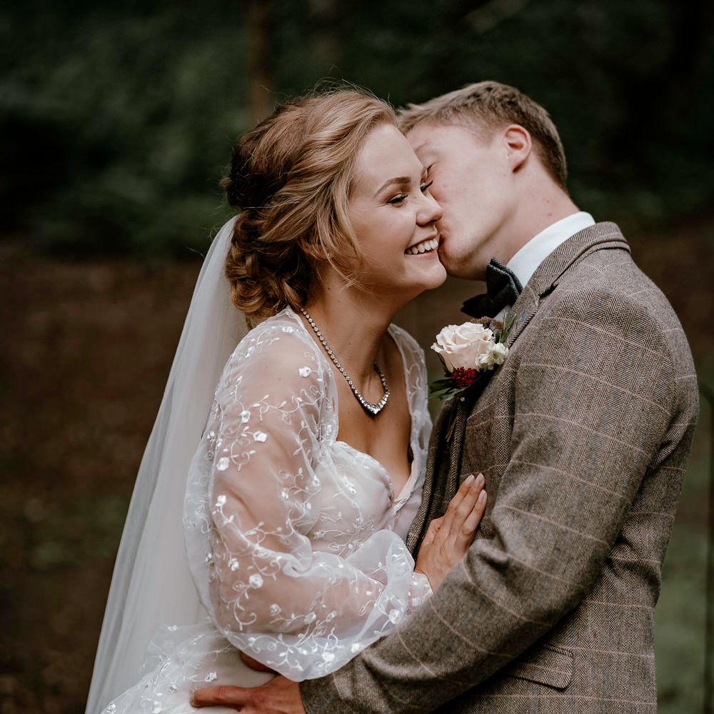 Groom in brown check suit kissing his bride at eco friendly wedding