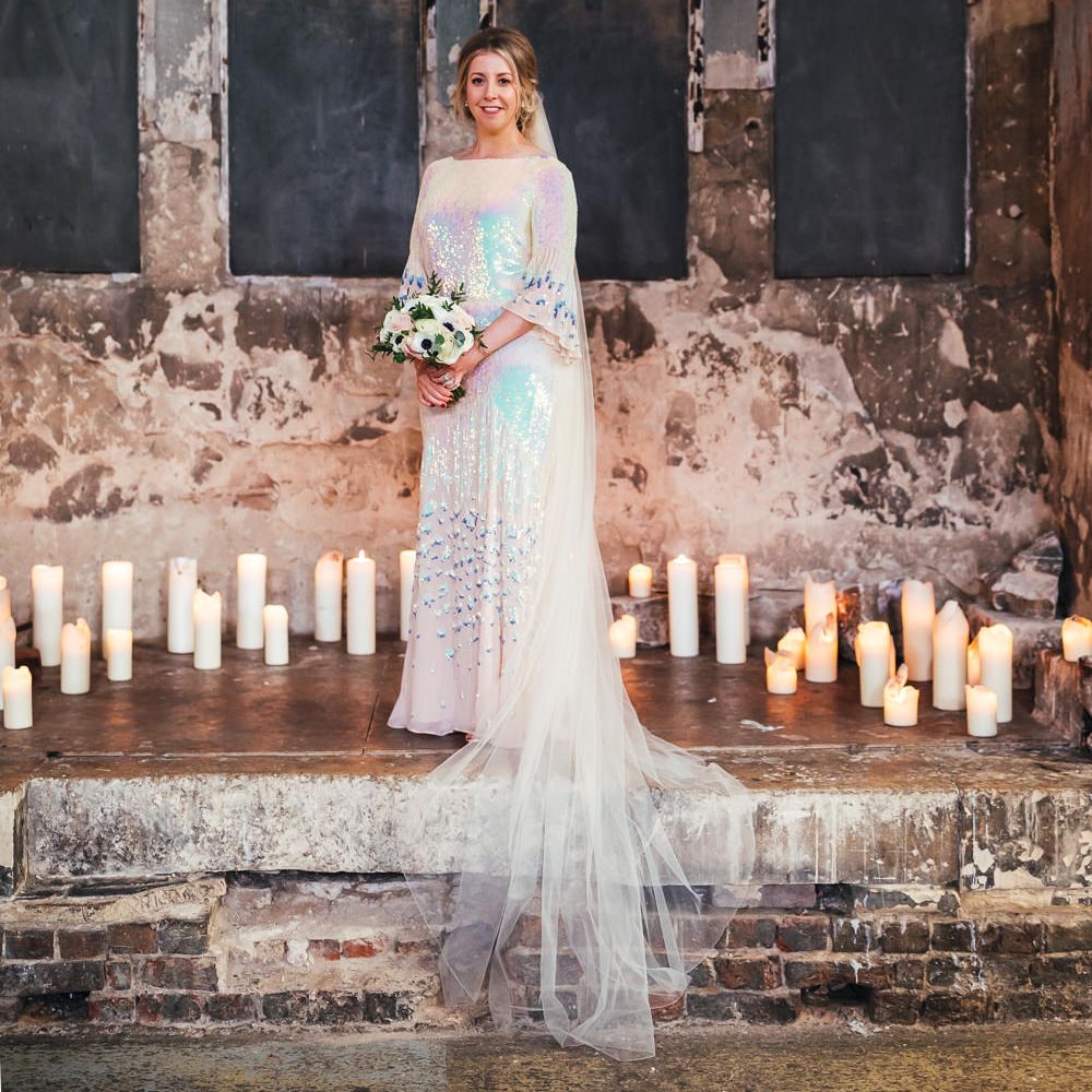 Bride wears iridescent wedding dress with floor length veil surrounded by candles