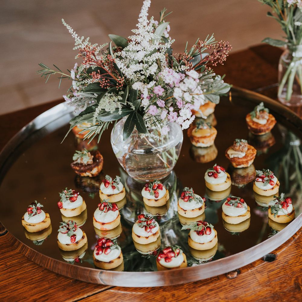 Canapés upon mirrored serving plate with floral bouquet in the middle 