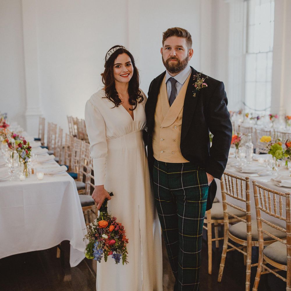 Bride and groom on their wedding day in London, bride wears long sleeved wedding dress with bright poppies and groom wears tartan trousers