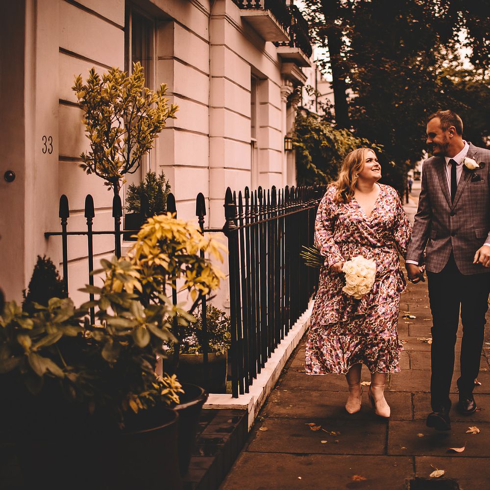 Bride & groom hold hands and walk through Chelsea together as bride carries classic white floral bouquet