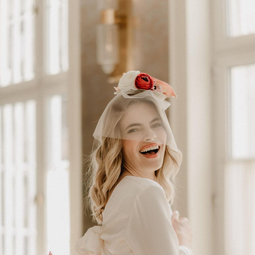Bride wearing a long sleeve mid length wedding dress with sequin skirt detail, and a short mesh veil covering her face with flowers on her head
