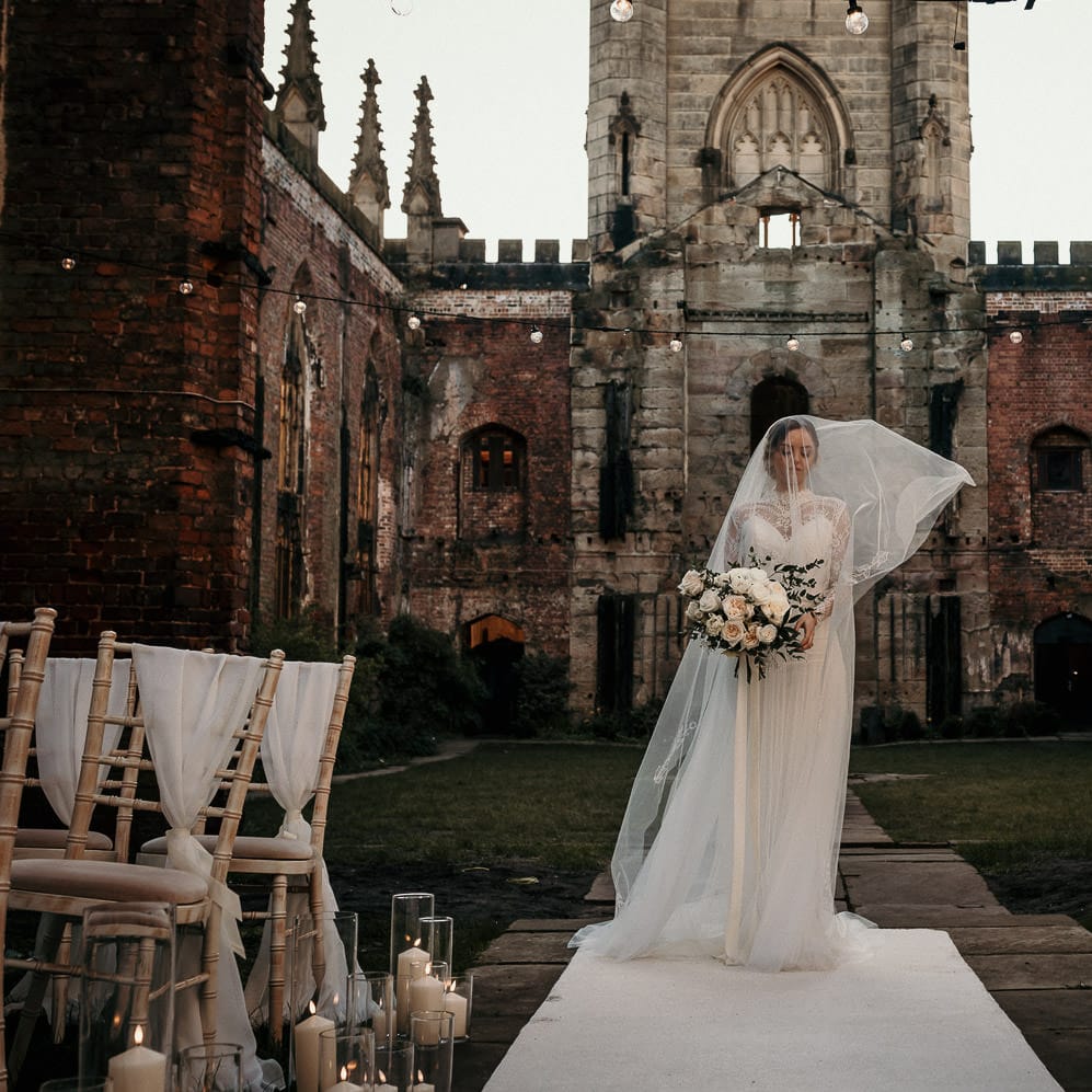 Bride in a lace dress and wedding veil standing at the top of the bomb out church altar 