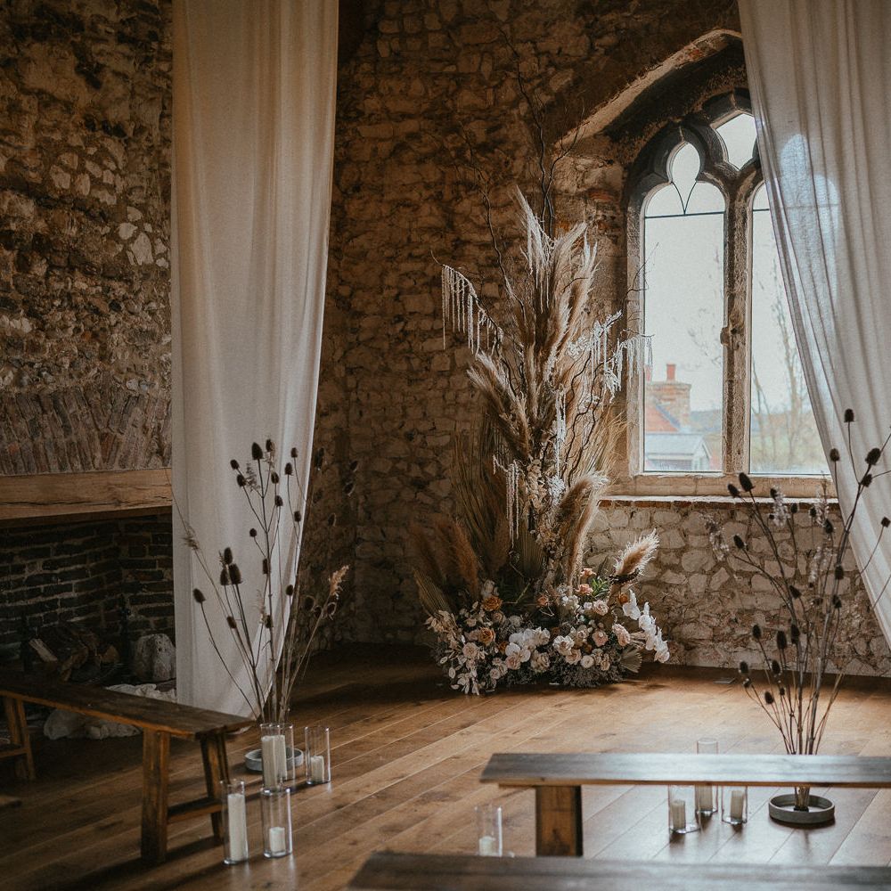 Rustic ceremony room at Pentney Abbey decorated with drapes and dried and fresh floral arrangements 