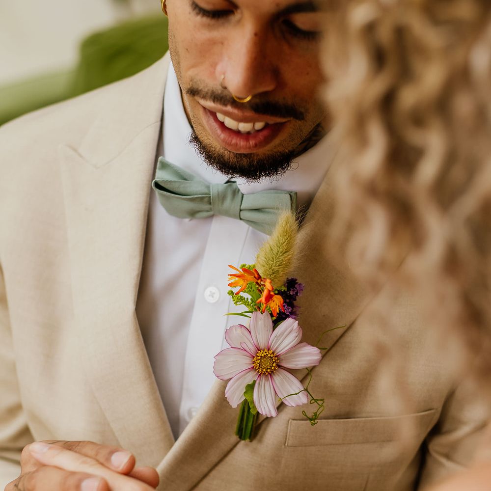 Groom in a beige suit with mint green bow tie and wildflower buttonhole 