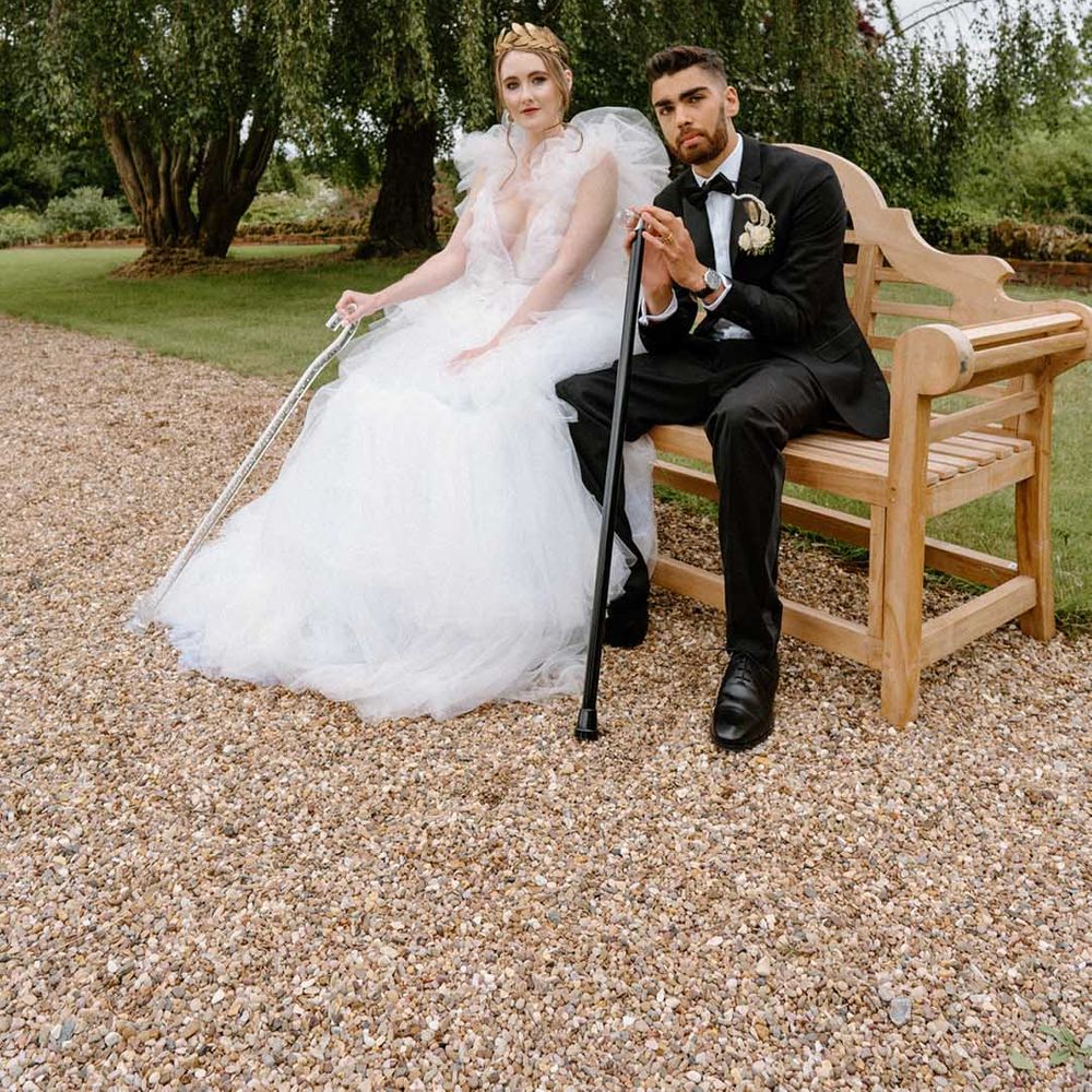 Interabled bride and groom sitting on a bench at Bourton Hall with their walking sticks wearing a tulle wedding dress and black tuxedo 