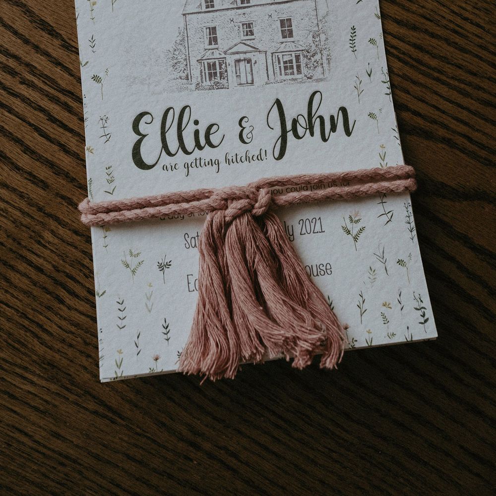 Wedding invite on white paper with house illustration and leaf prints tired with pink rope for Isle of Wight wedding with macrame wedding decor