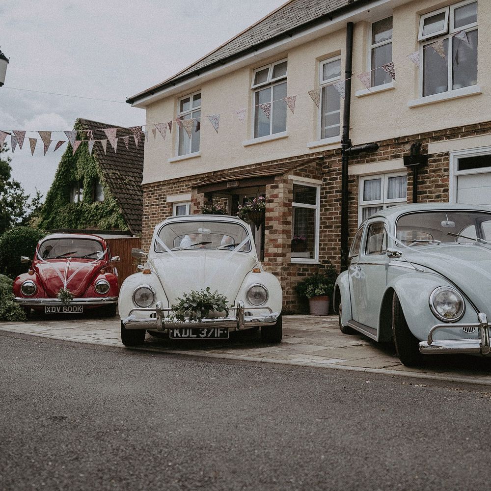 Three VW bugs decorated for wedding with ribbon and florals parked outside house before Isle of Wight wedding with macrame wedding decor