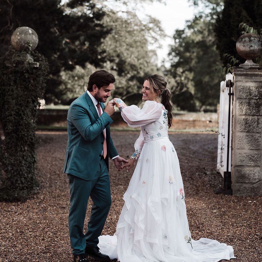 Groom in blue suit and pink tie kisses hand of bride in long mesh sleeve wedding dress with train at Iscoyd Park