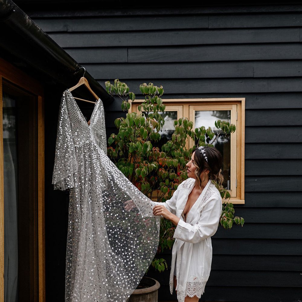 Bride in a satin getting ready robe with lace trim looking at there Silver, sequin, Chosen By Kyha wedding dress 