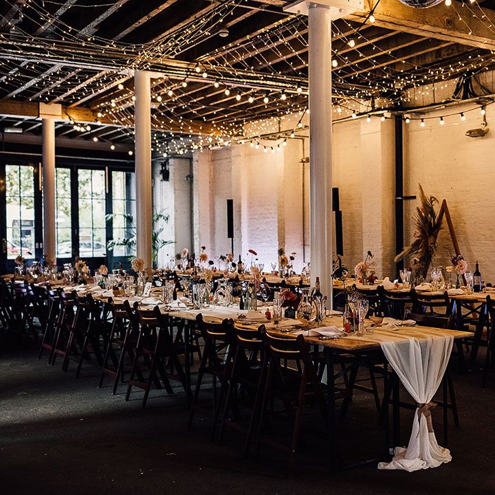 Industrial wedding reception decor at 100 Barrington with fairy light canopy, table runners and flower stems in bottles table decor 