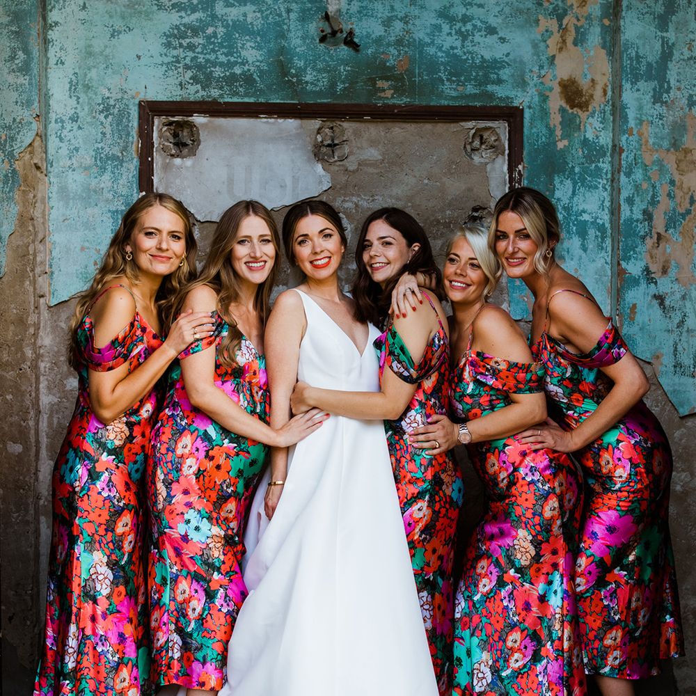 Bride huddles with her bridesmaids in bright green, pink, blue and red floral dresses 