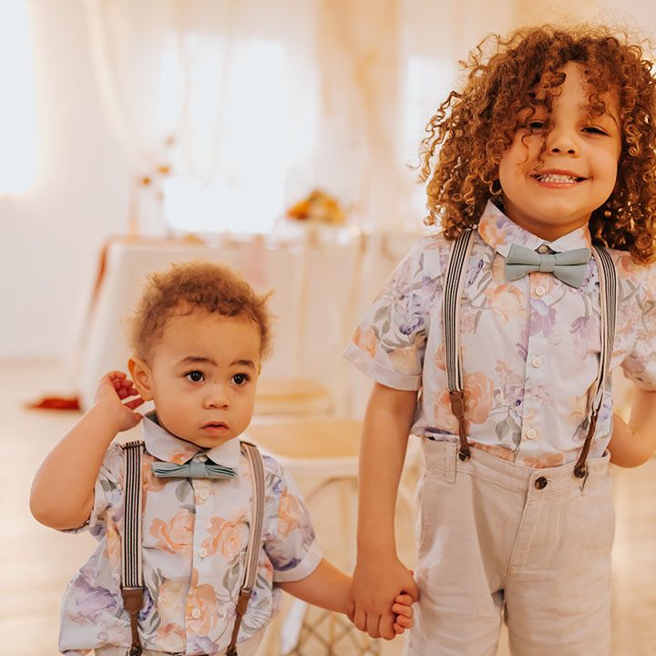 Adorable page boys with naturally curly hair in shorts, braces, bow ties and floral shirts 