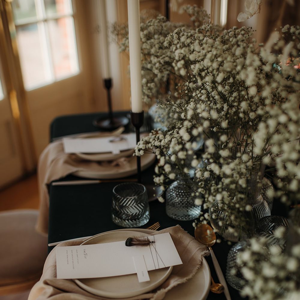 Place setting with black table cloth, gypsophila centrepiece decor and menu cards with feathers 