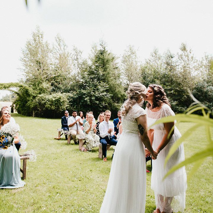 Brides share their first kiss as a married couple as wedding guests clap at outdoor ceremony