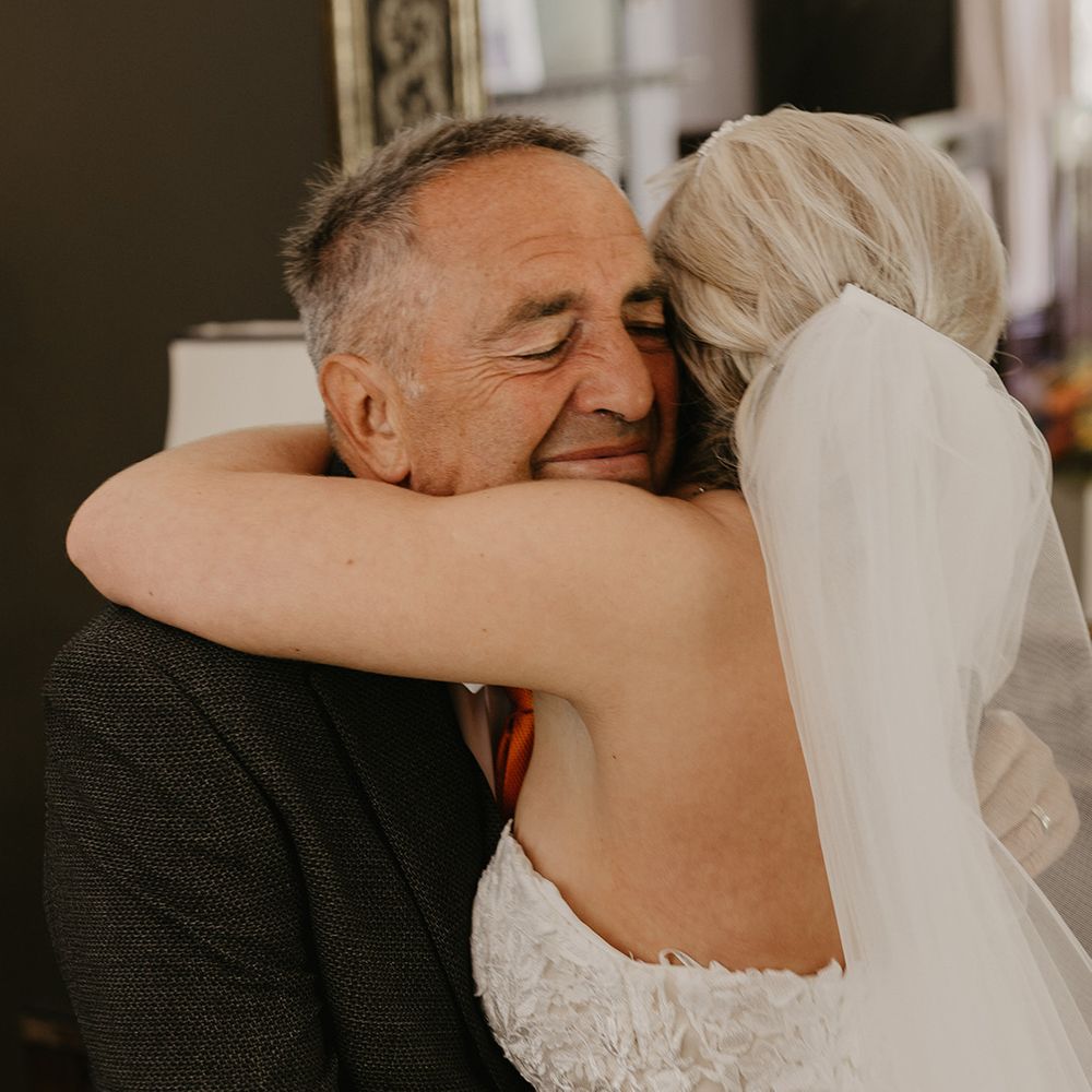 Bride in strapless lace wedding dress hugs her father in dark suit jacket 