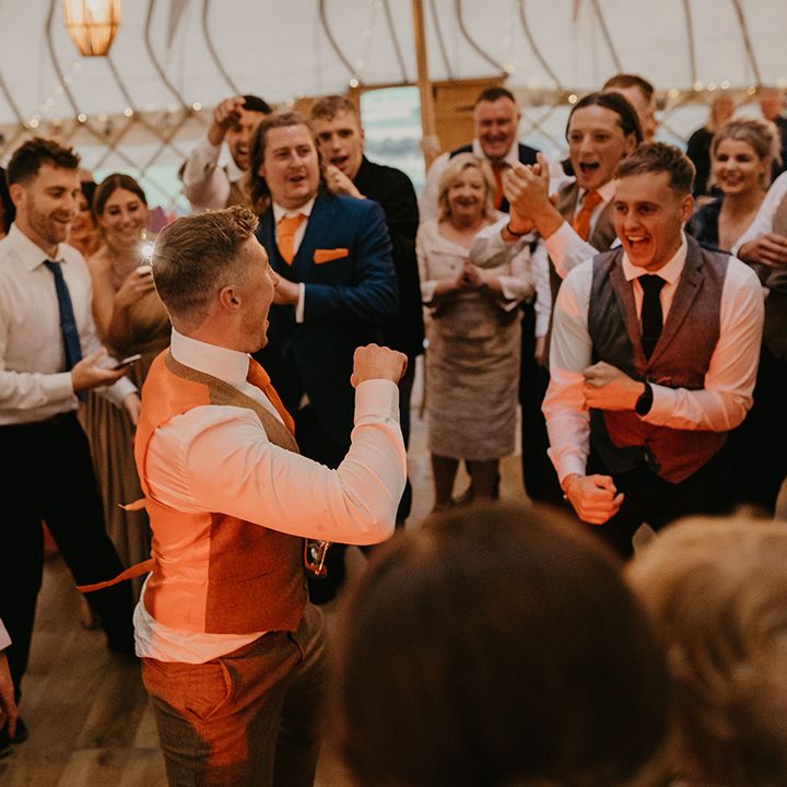 Wedding guests form a circle around the groom as he dances during the wedding reception