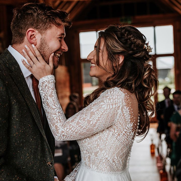 Bride in sheer lace illusion top wedding dress holding the groom's face wearing green wool suit