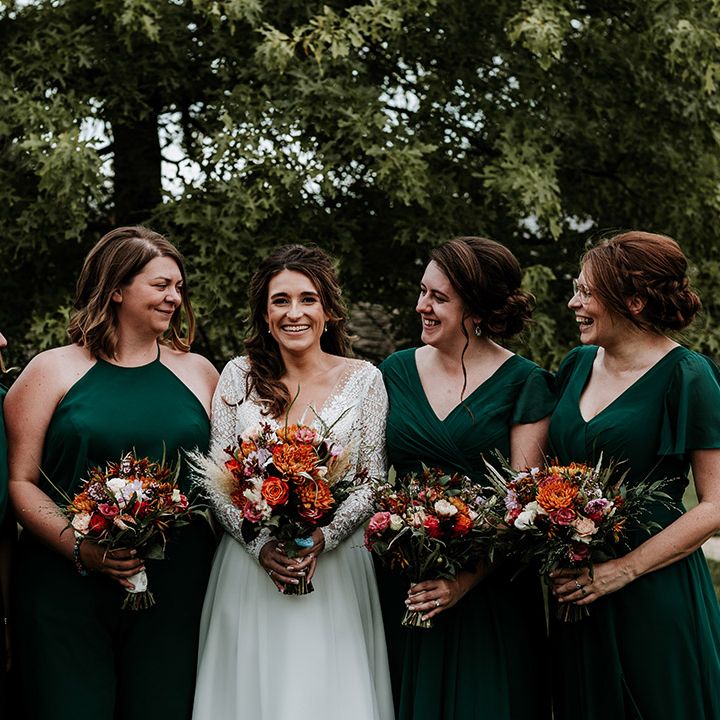 Bride in sheer lace illusion top wedding dress with long sleeves standing with bridesmaids in emerald green dresses