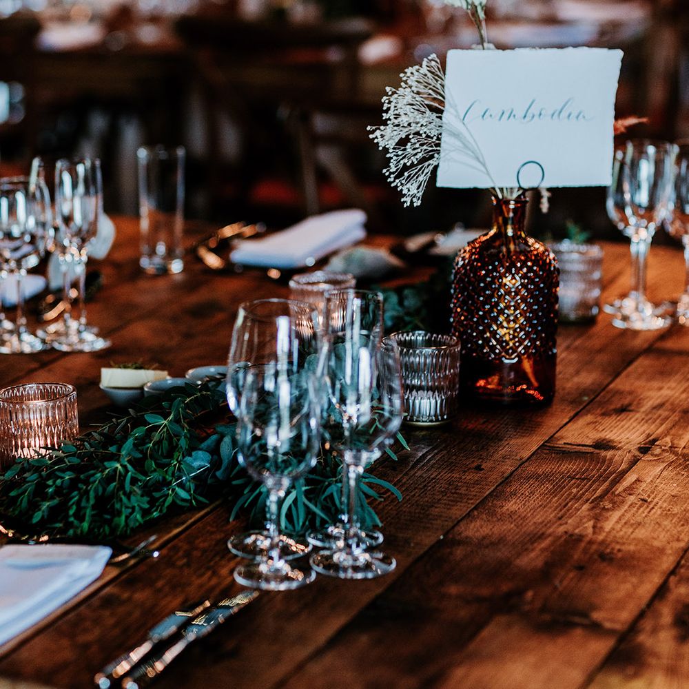 Coloured glass vases on dark wooden tables with leaf runners and small candle holders 