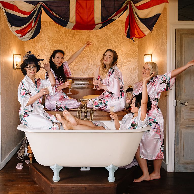Bride with bridesmaids and mother of the bride in pink and white flower satin robes while they get ready for the wedding 
