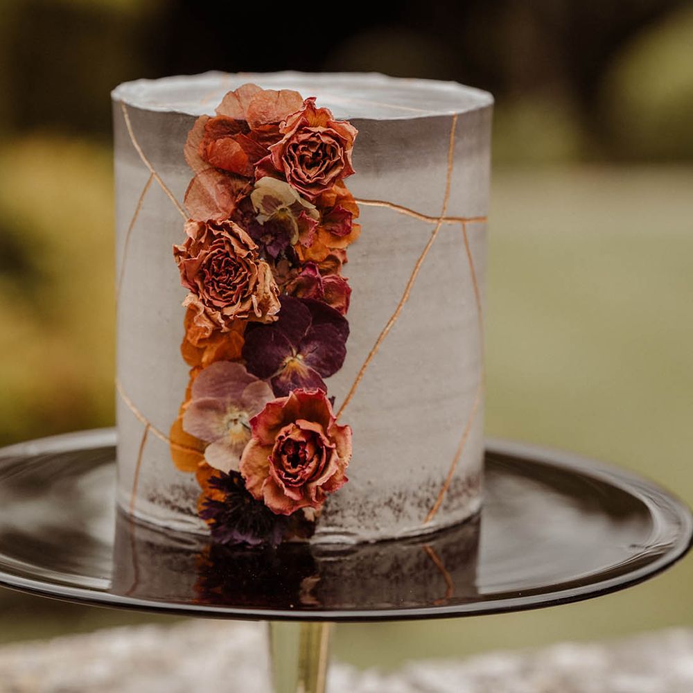 Single tier grey marble effect wedding cake with orange wedding flowers on a black cake stand 