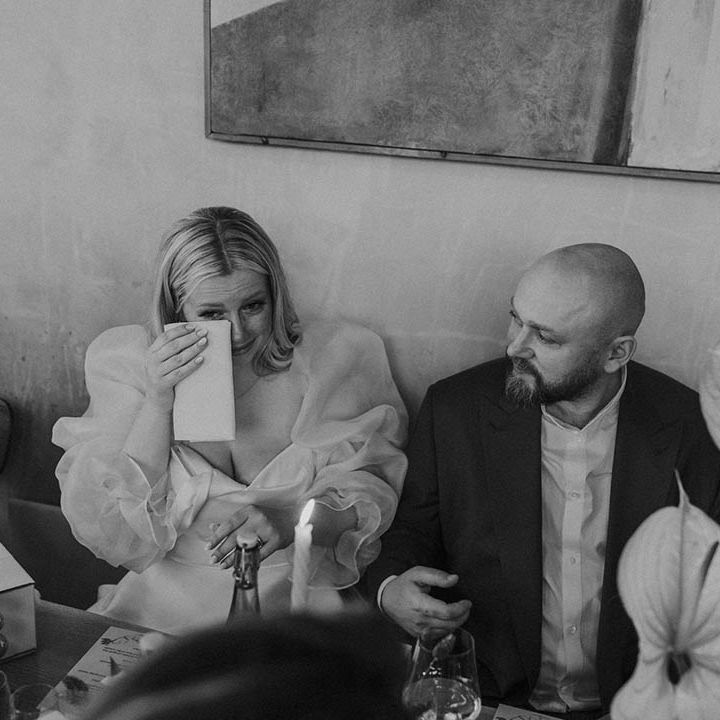 bride in a Jesus Peiro wedding dress with sheer long voluminous sleeves wiping tears from her eyes at her wedding reception 