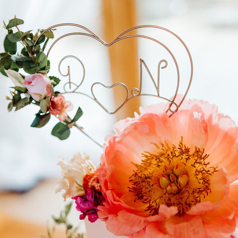 Pink frosted wedding cake finished with personalised silver cake topper and brightly coloured floral decor in shades of coral and pink