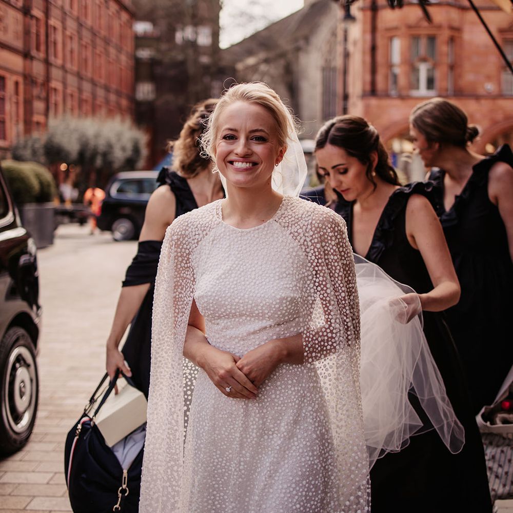 Bridesmaids in black dresses help the bride get out of the car in her sparkly outfit 