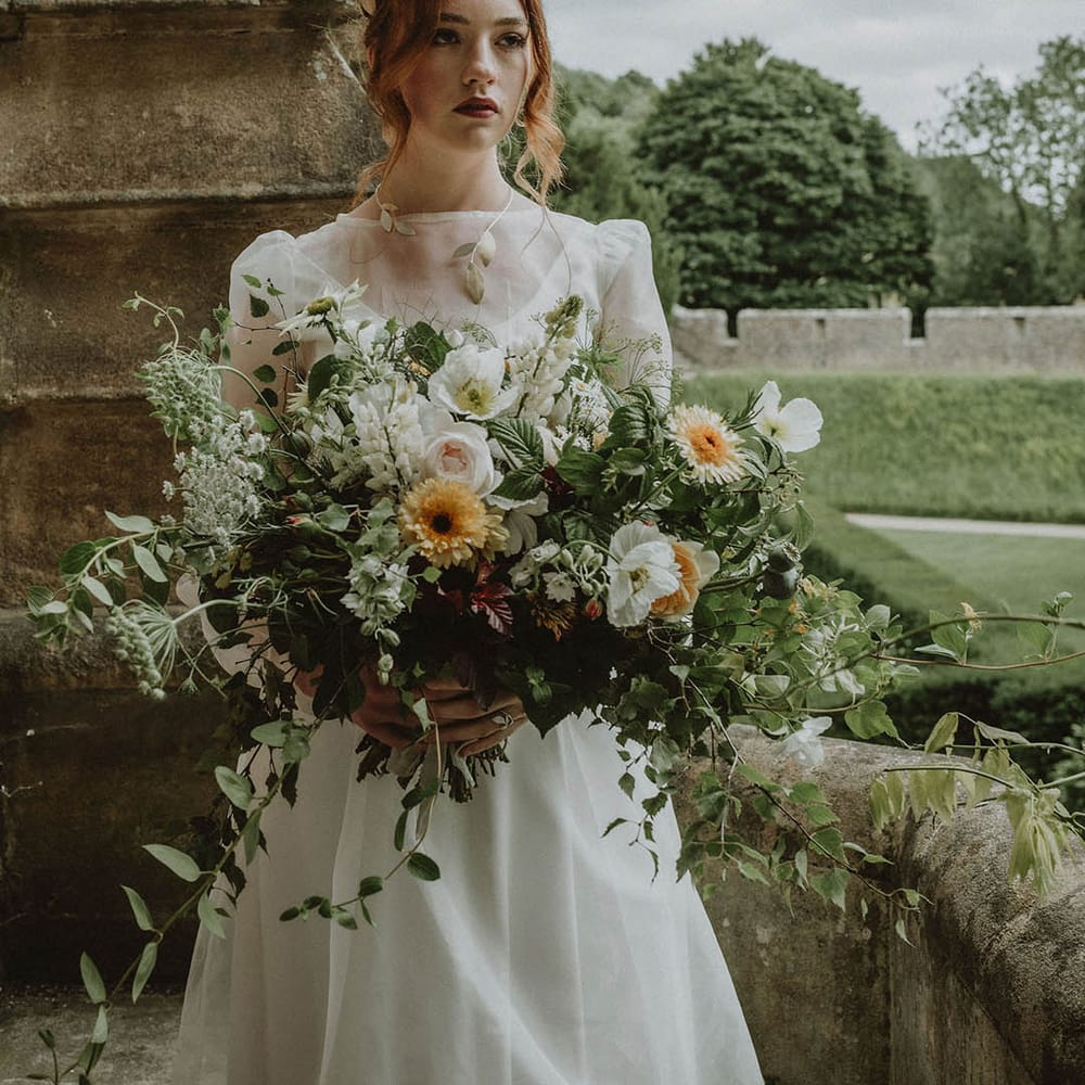 Bride wearing a gold leaf headpiece holding an oversized bridal bouquet with green foliage and white and yellow flowers 