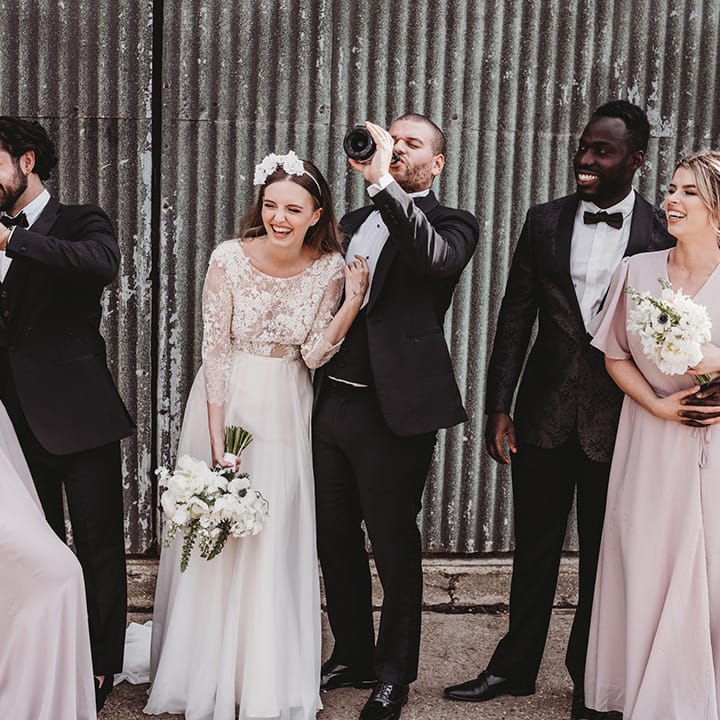 Wedding party laugh and smile together as they all drink champagne 