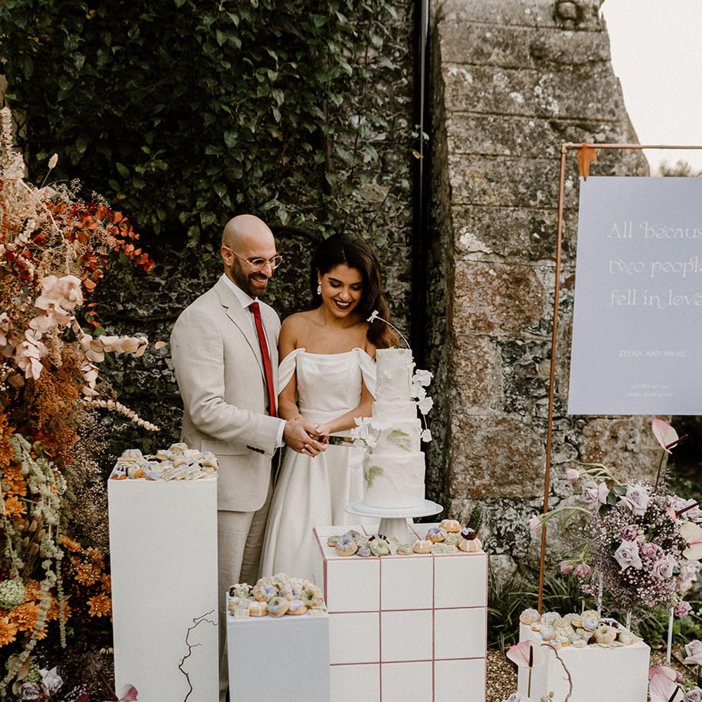 Bride and groom cut their four tier wedding cake surrounded by mini desserts and a lavender and white wedding sign 
