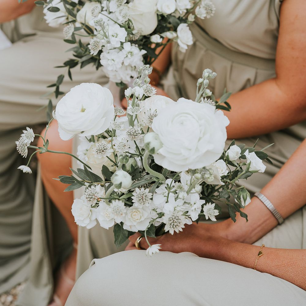 Bridesmaids in sage green dresses holding pure white wedding flowers 