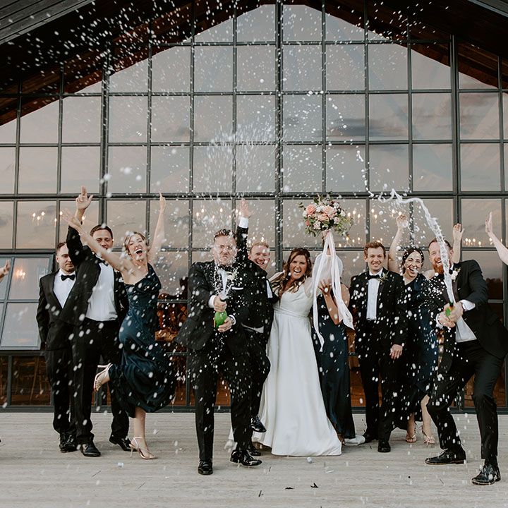 Bride & groom stand with their wedding party during champagne spray outdoors