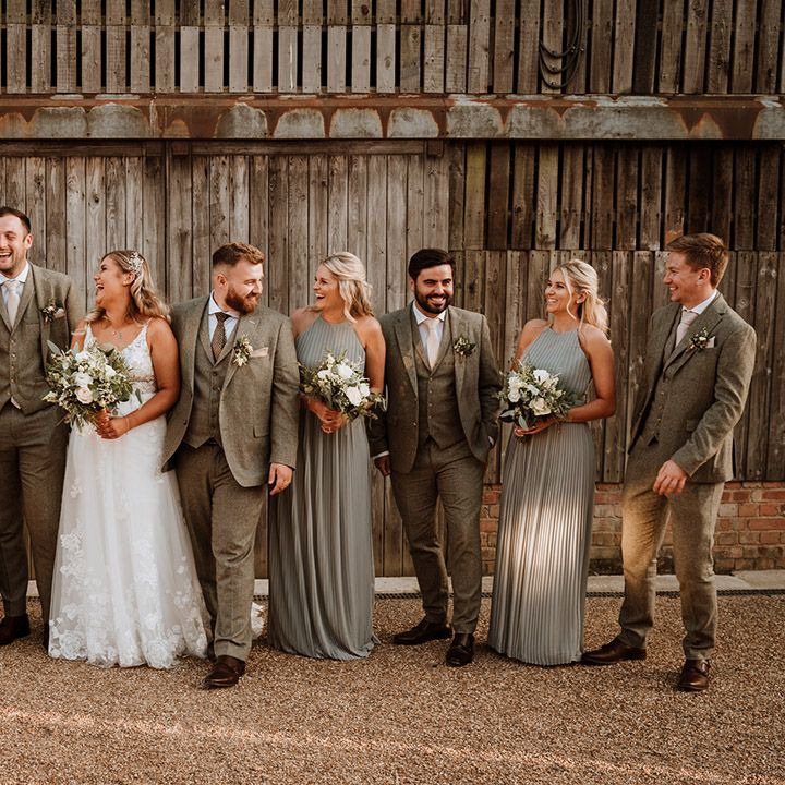 The wedding party with the groom and groomsmen in grey suits, each bridesmaid in a sage tree pleated bridesmaid dress, and the bride in a lace wedding dress