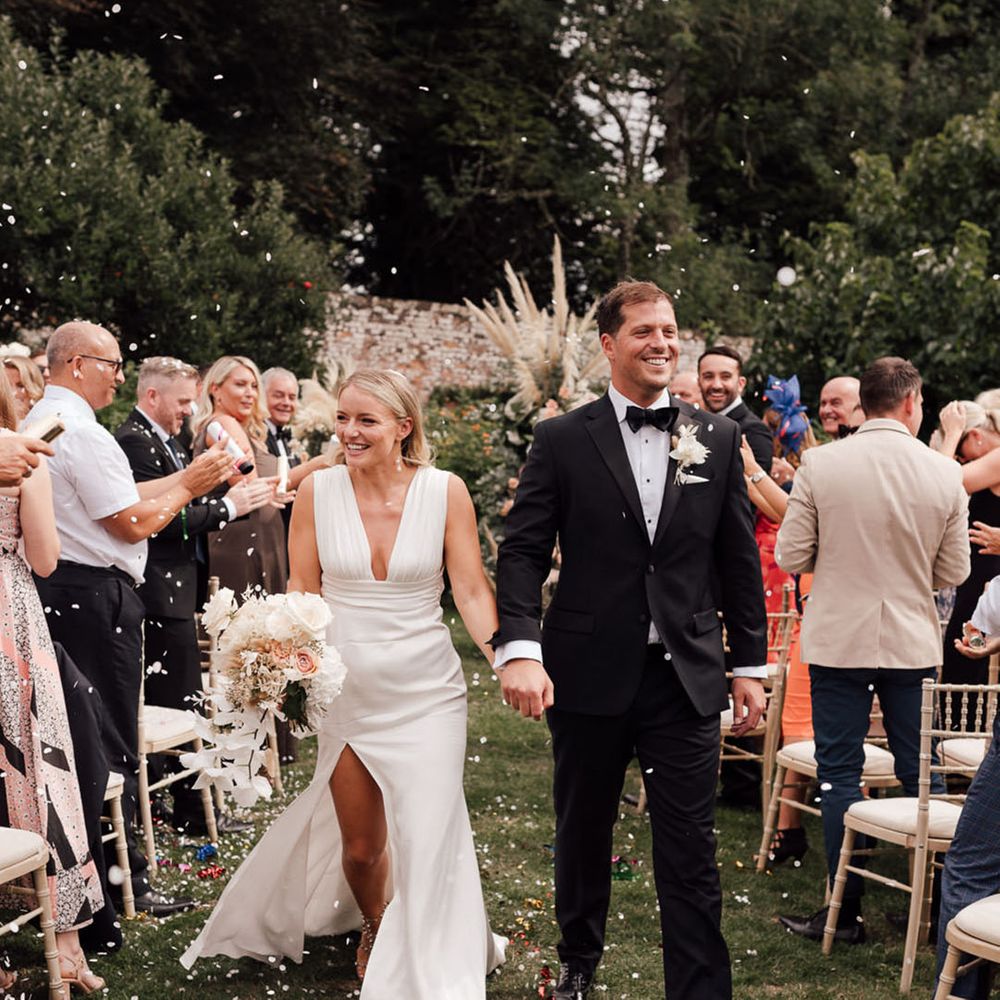 The bride and groom walk back down the aisle with confetti 