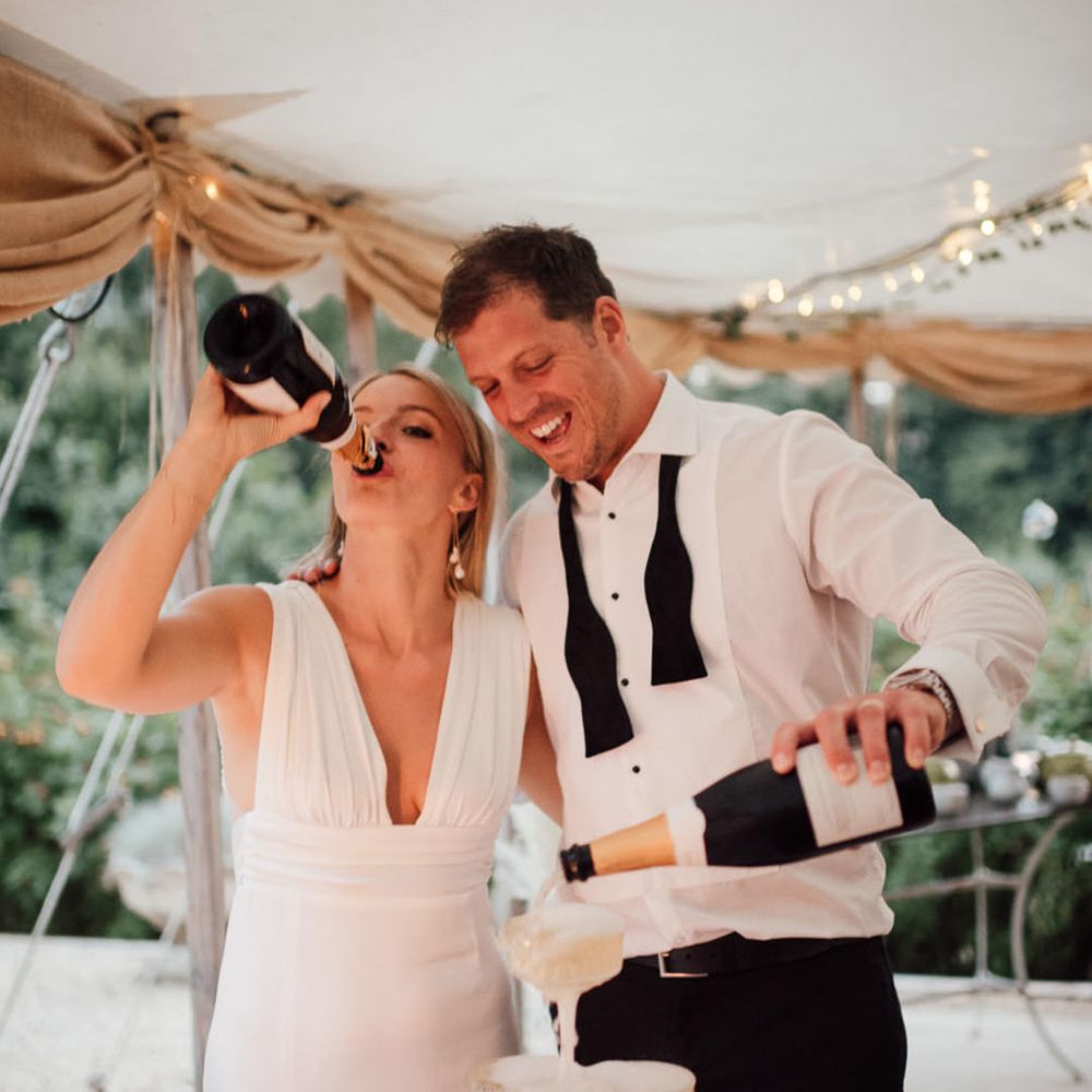 The bride and groom pour champagne for their champagne tower as the bride drinks from the bottle 