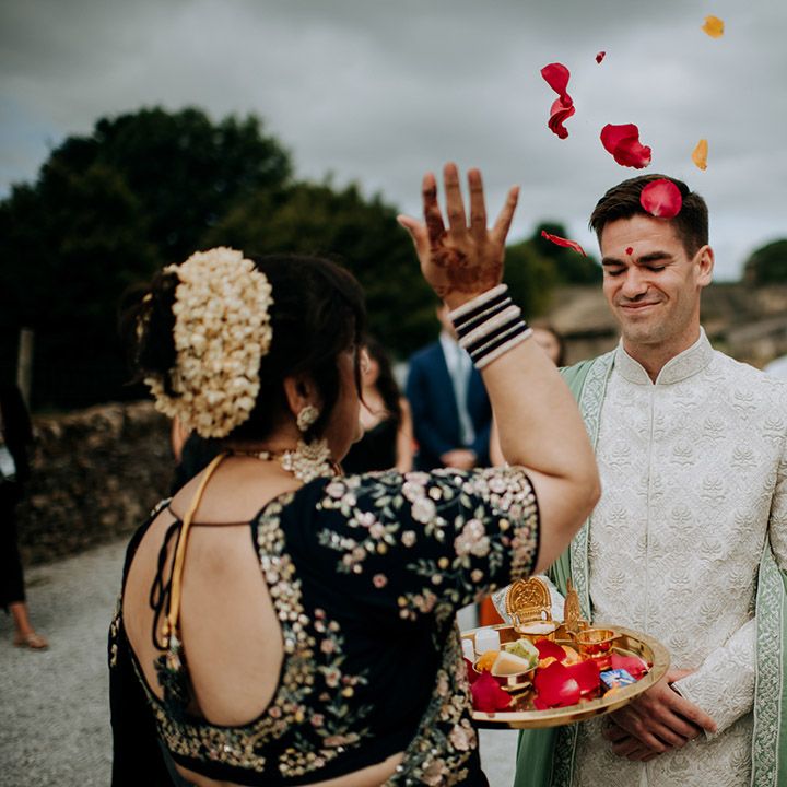 Groom has colourful petal confetti thrown towards him outdoors during Haldi ceremony