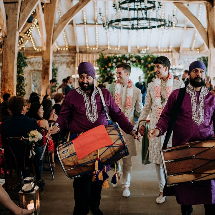 Grooms wear matching lei's and walk down the aisle as drummers wearing deep purple sherwani's play 