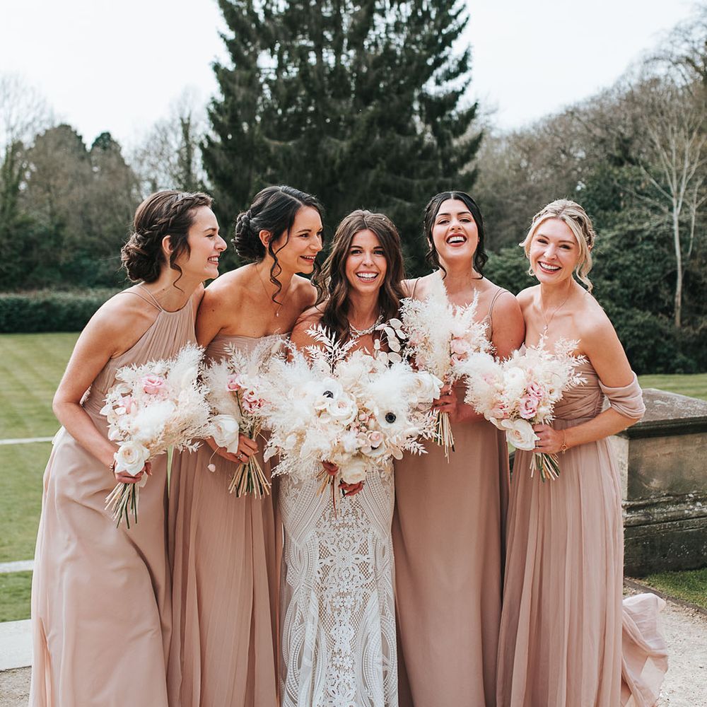Bridal party shot with the bridesmaids wearing matching hairstyles and matching colour neutral pink dresses in different styles with the bride 