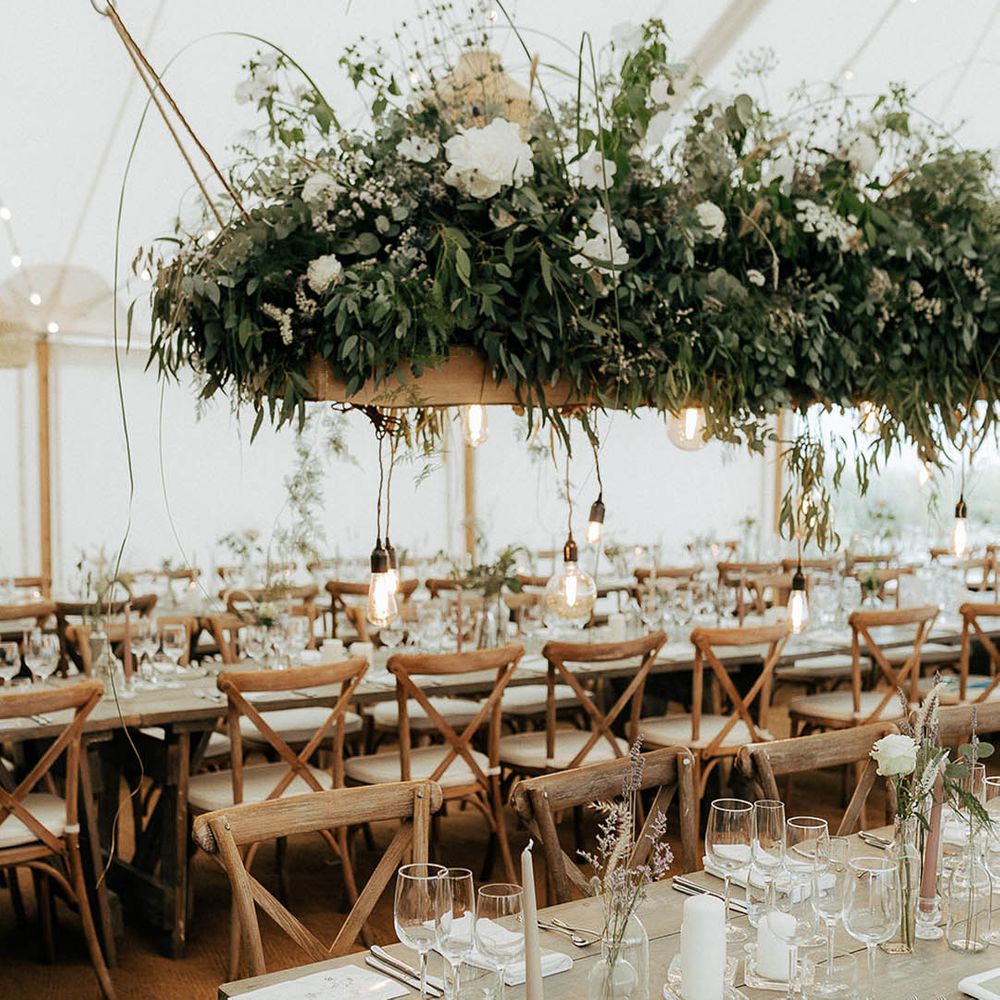Marquee wedding reception with wooden banquet tables, green foliage hanging installations and fairy light canopy