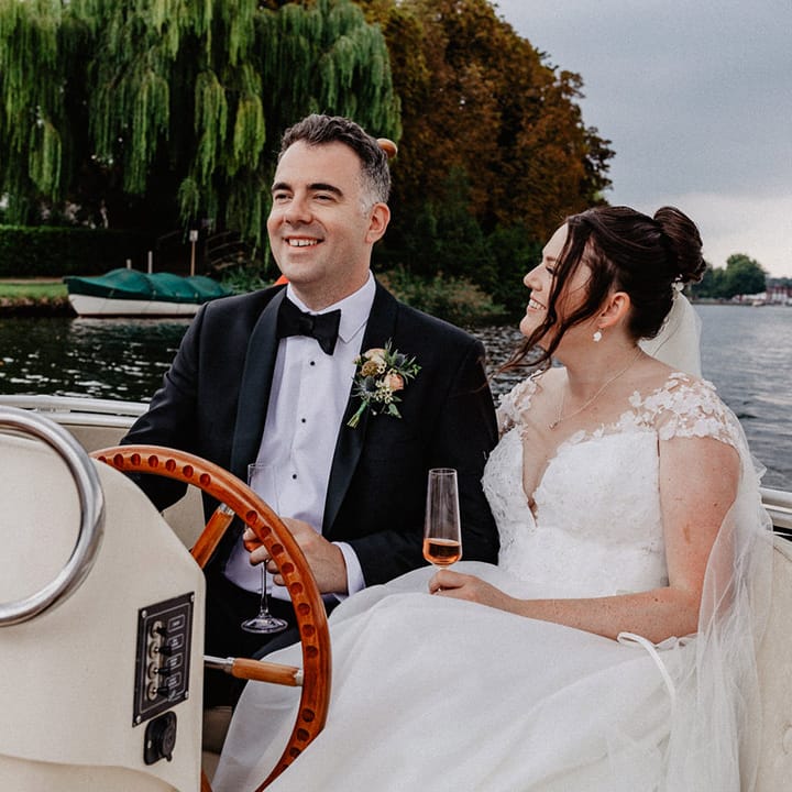 The groom drives the boat around with the bride in a Suzanne Neville wedding dress at Henley on Thames 
